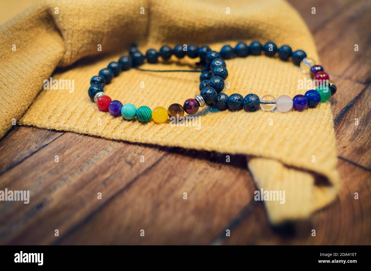 two stone bracelets for healing crystal therapy, with lava stones and different crystals on a wooden table and yellow cloth Stock Photo