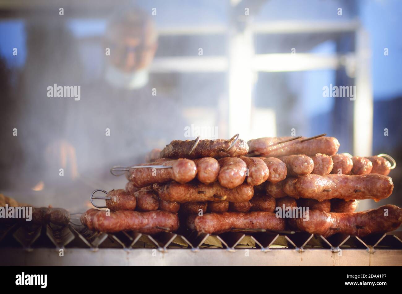 man grilling traditional italian sausages on a street food market stall at evening with light