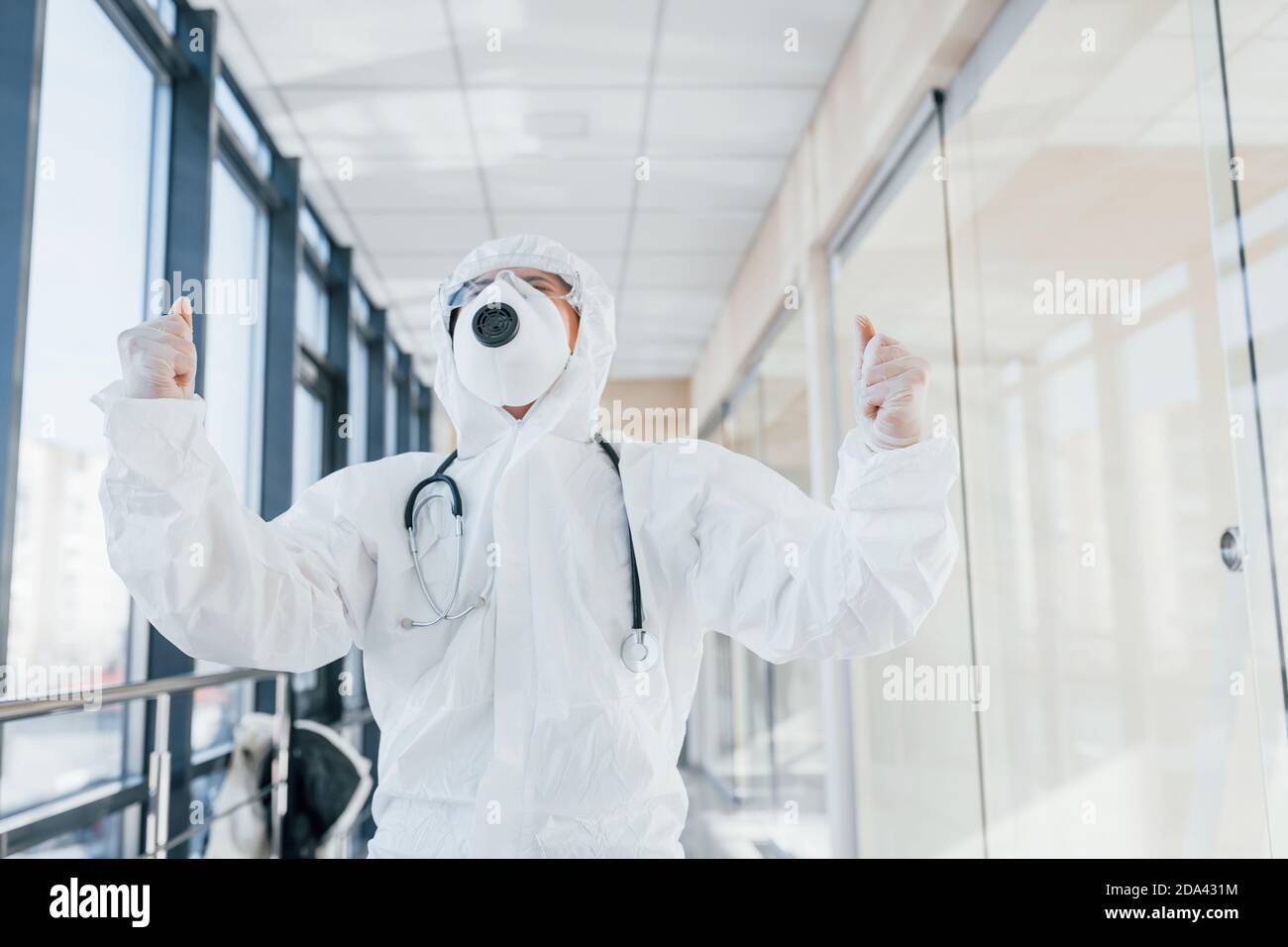 Celebrating victory. Female doctor scientist in lab coat, defensive eyewear and mask standing indoors Stock Photo
