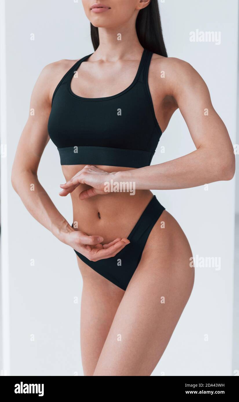 Slender woman in black fitness underwear standing indoors in room at daytime Stock Photo