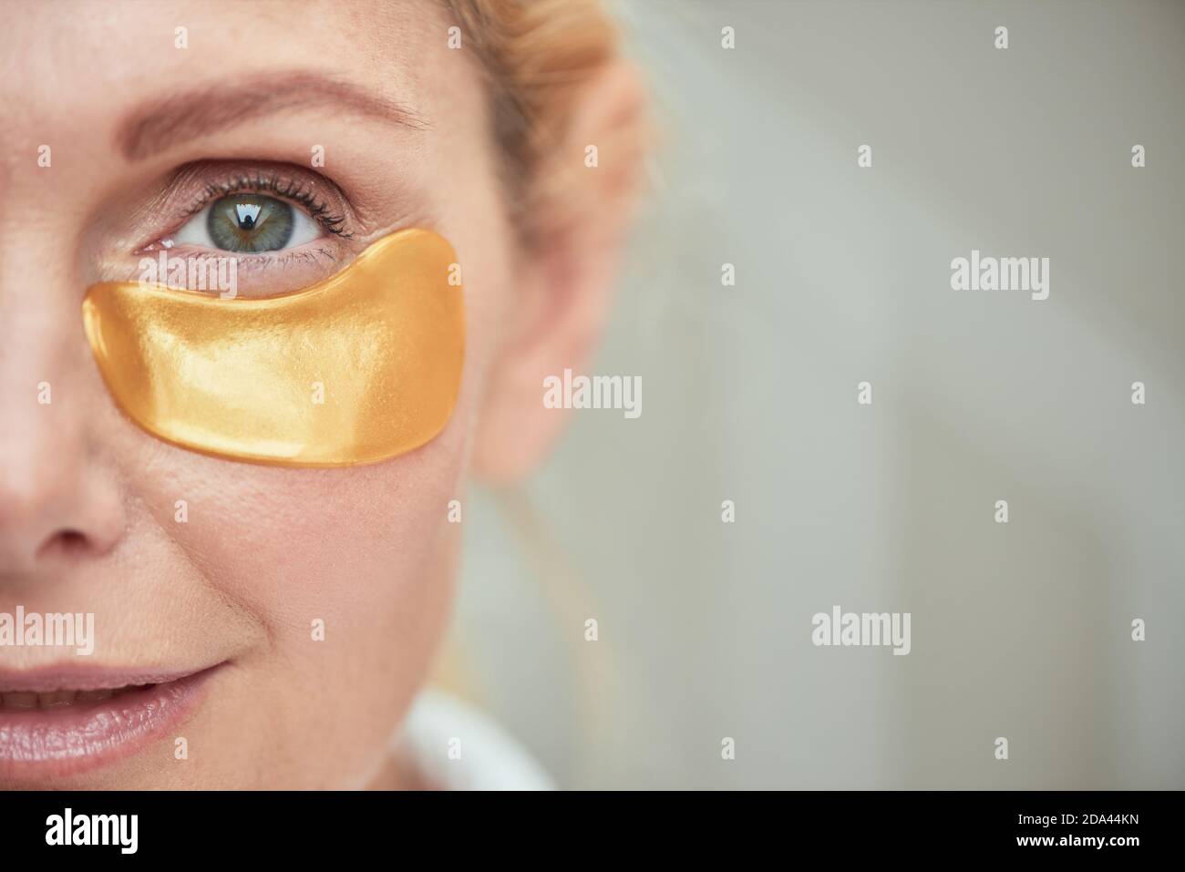 Under eye patch on smiling middle aged caucasian woman face, selective focus. Beauty, skincare and cosmetology concept Stock Photo