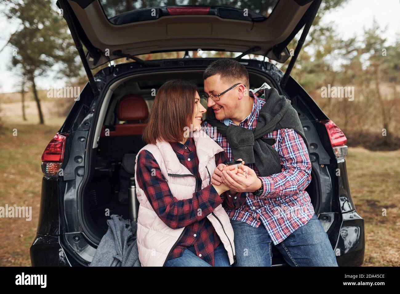 Happy mature couple sitting together on the back of a car outdoors in forest Stock Photo