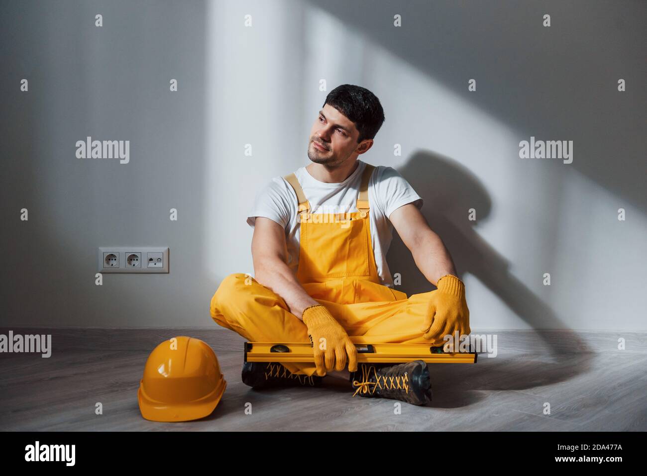 Tired handyman in yellow uniform sits indoors and takes break. House renovation conception Stock Photo