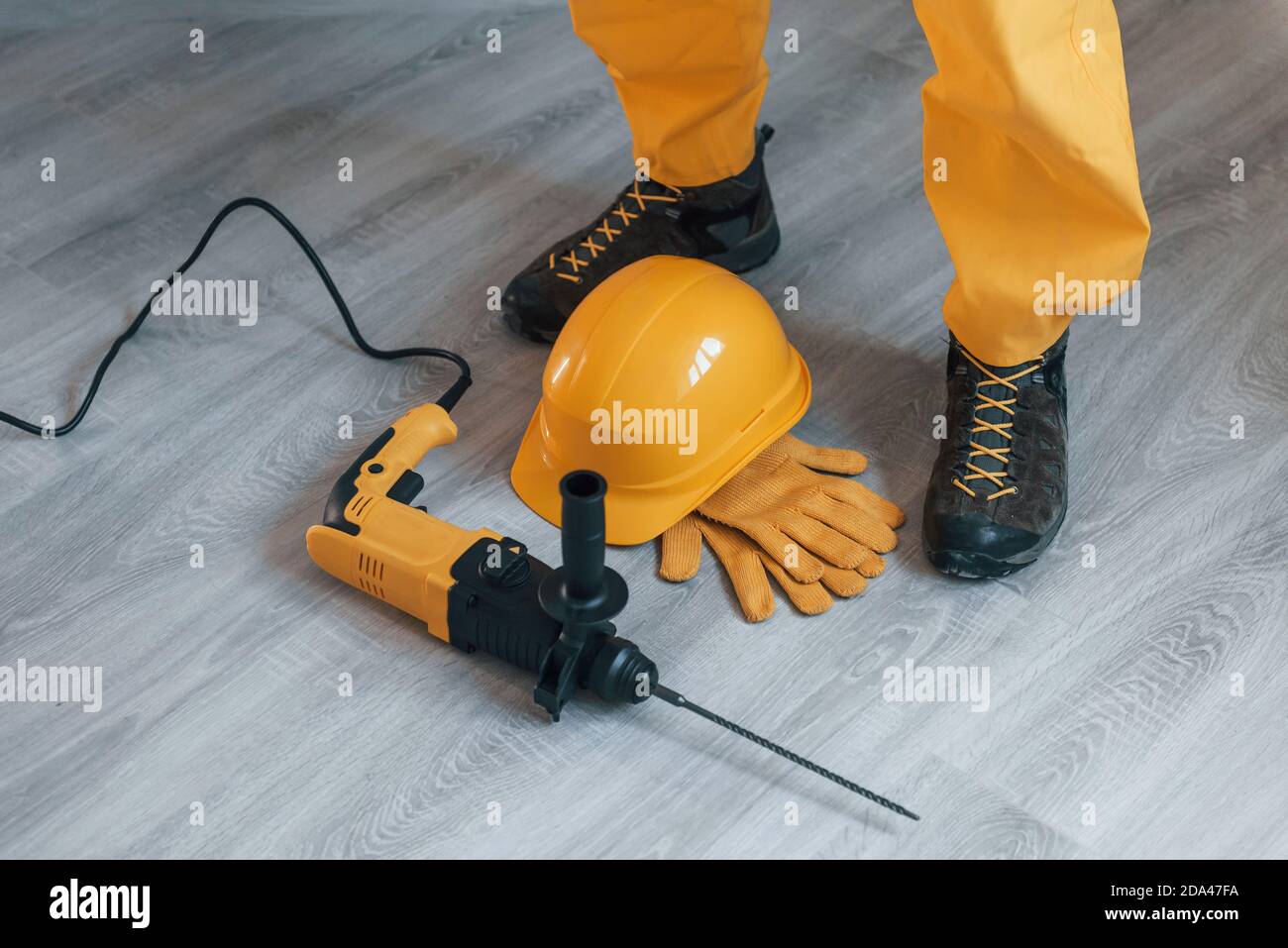 Handyman in yellow uniform with drill standing indoors. House renovation conception Stock Photo