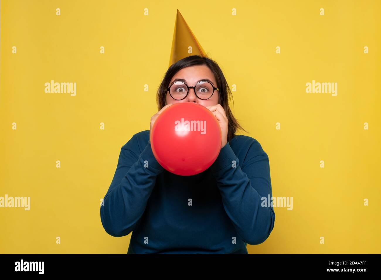 Caucasian woman in party hat blowing up red balloon Stock Photo
