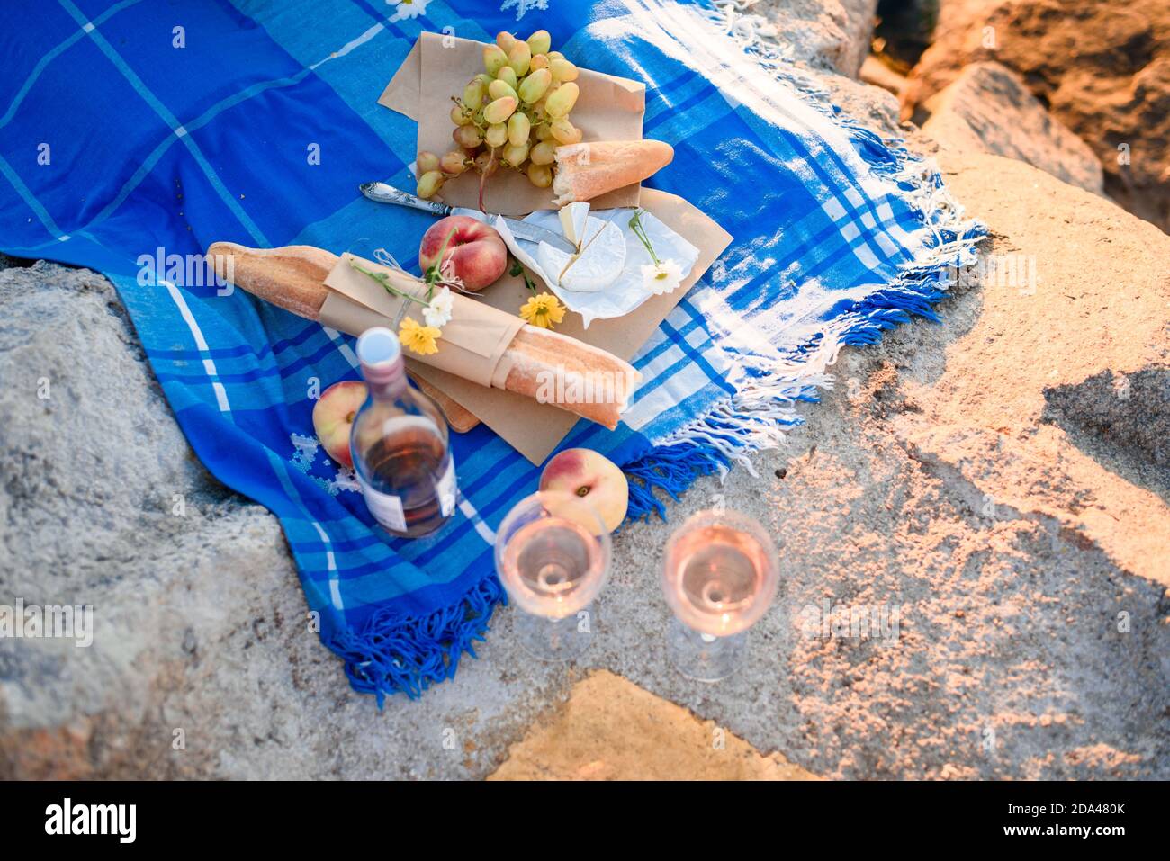 Summer romantic picnic for two at the burega sea, with fruit, cheese, wine, bread, grapes, peach. Light from the first rays of the sun. Picnic at dawn Stock Photo