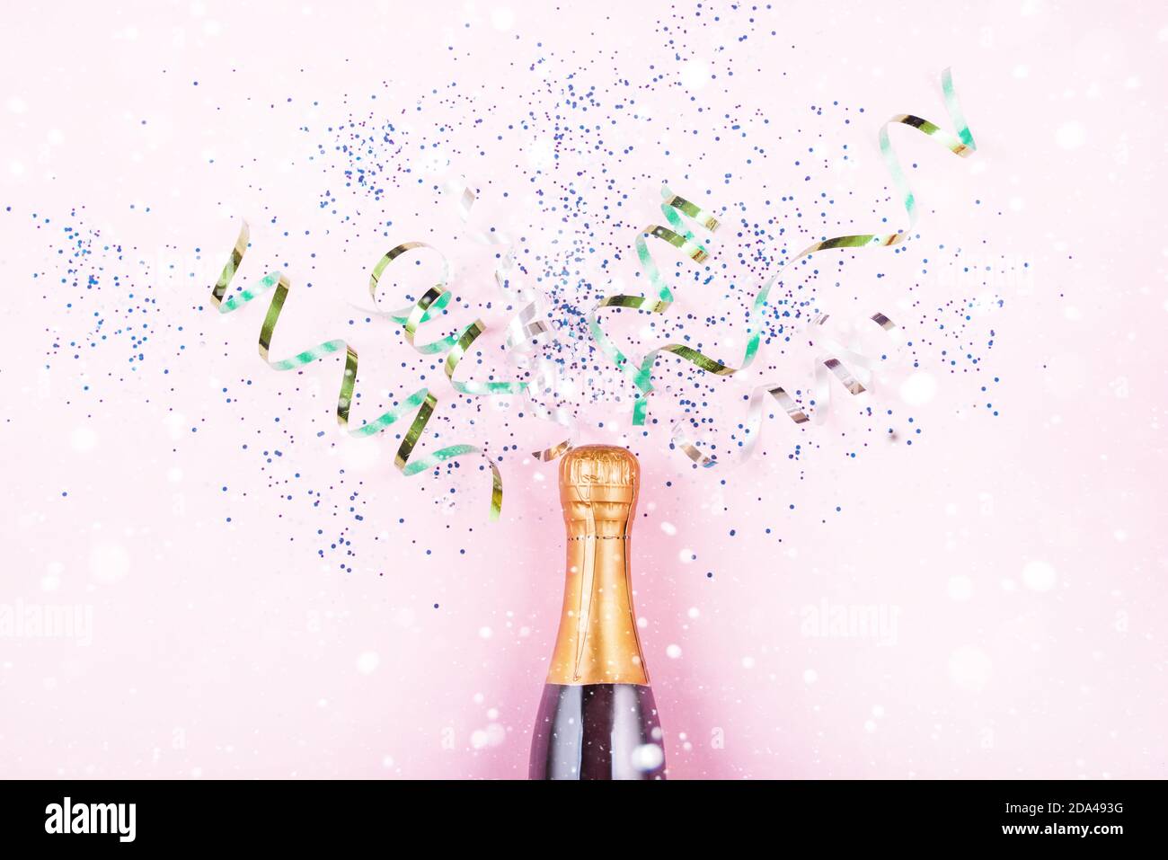 New Year's serpentine flies out of the bottle of champagne, multicolored sequins on a light background. New Year's content 2021. Flat lay Stock Photo