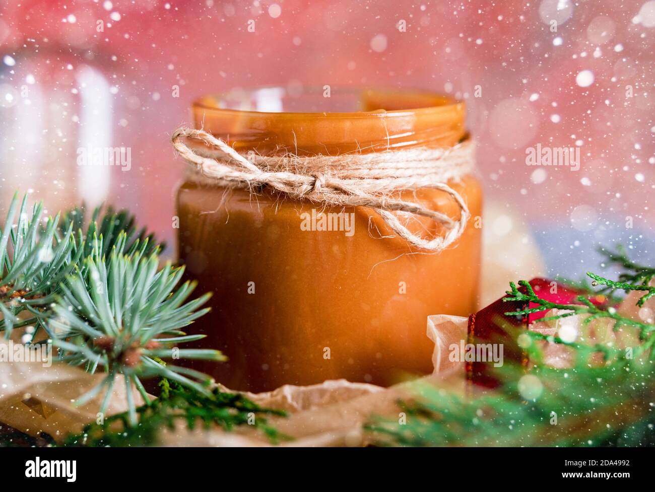 A small jar with boiled homemade condensed milk. Shortbread Christmas cookies, lights, sprigs of spruce, bumps. New Year's content. Stock Photo