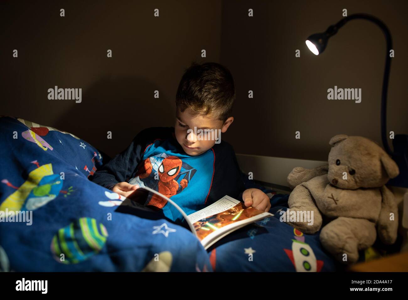 6 year old boy reading whilst lying in bed at bedtime at home, England