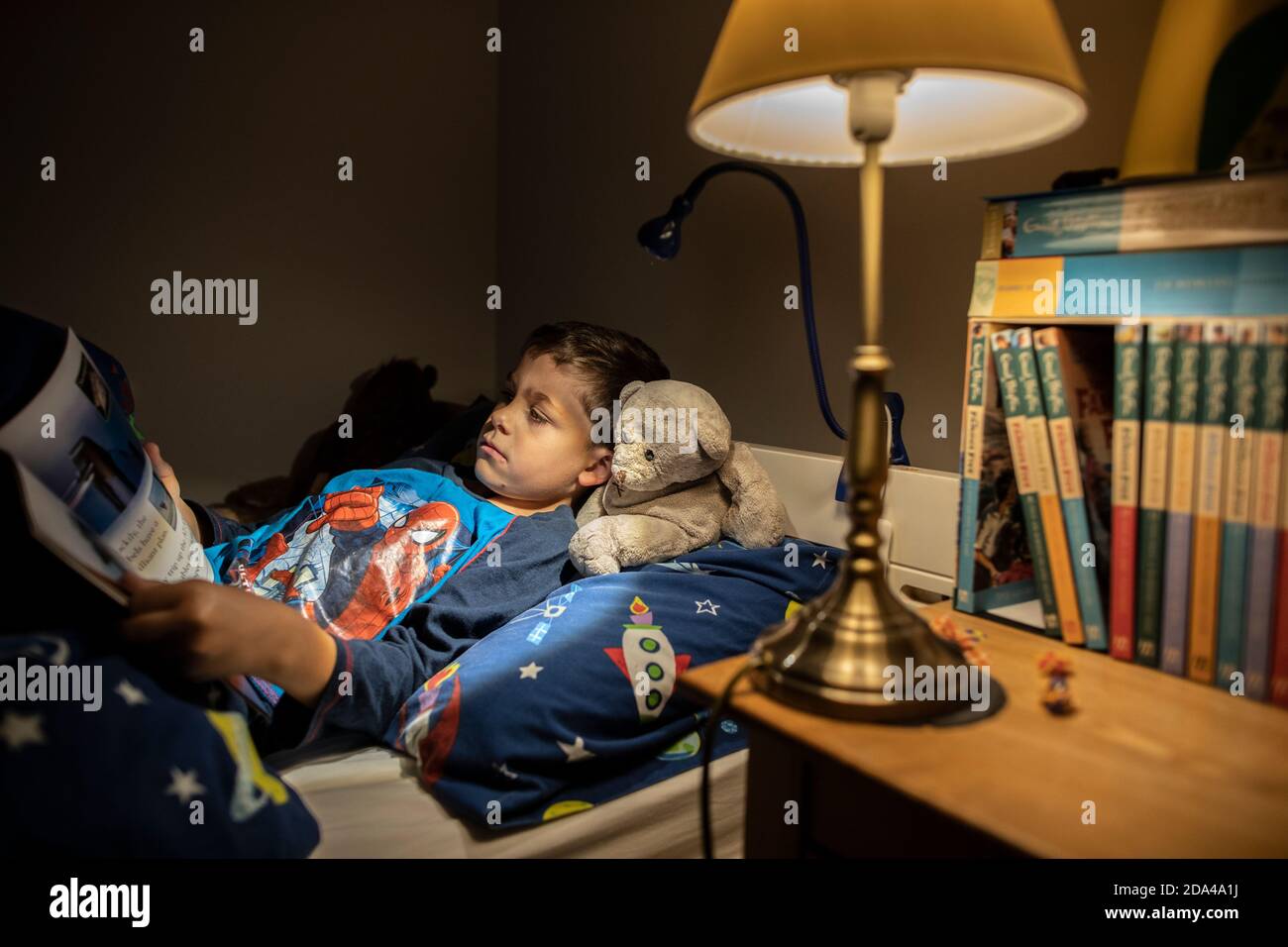 6 year old boy reading whilst lying in bed at bedtime at home, England