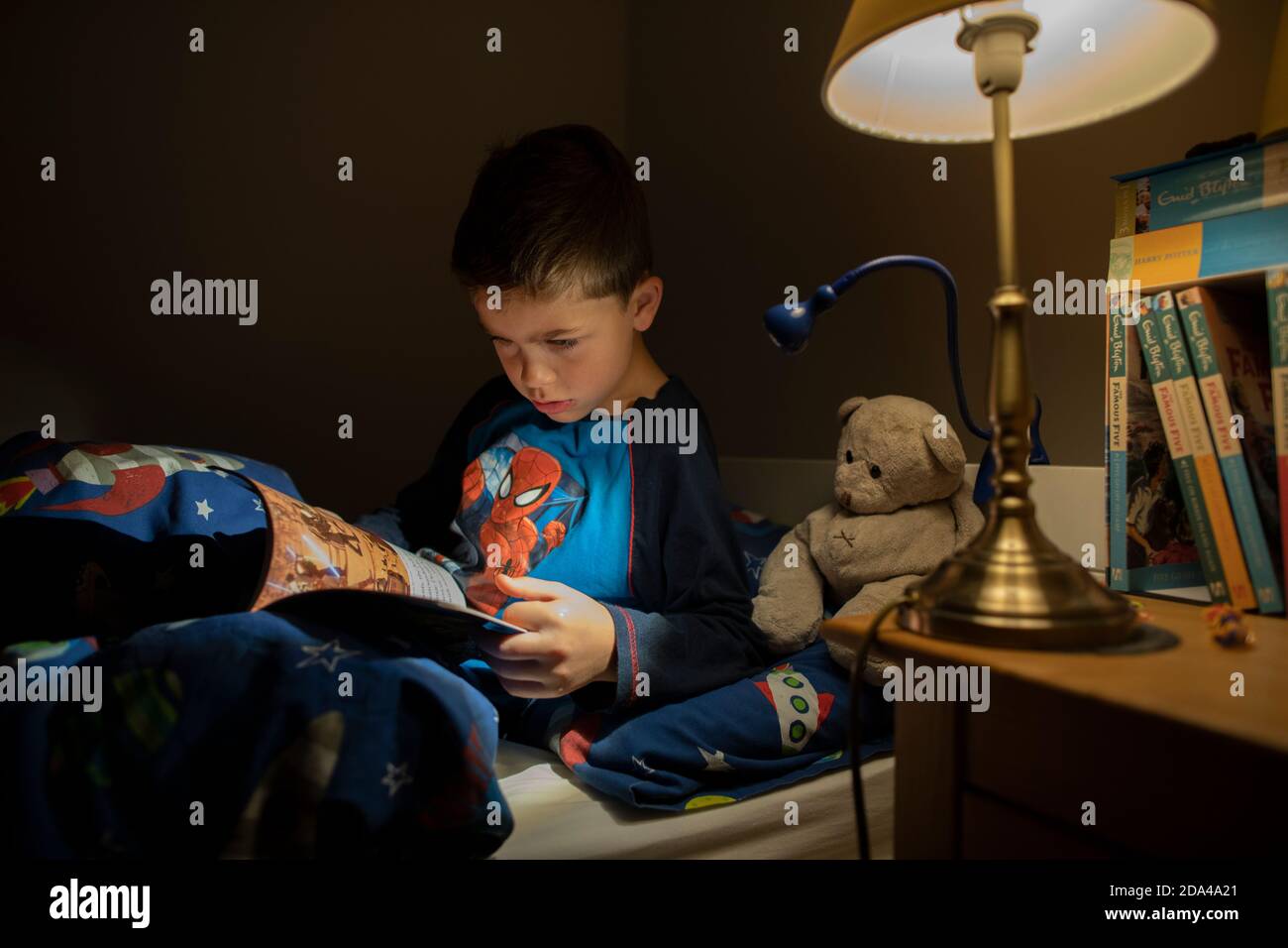 6 year old boy reading whilst lying in bed at bedtime at home, England