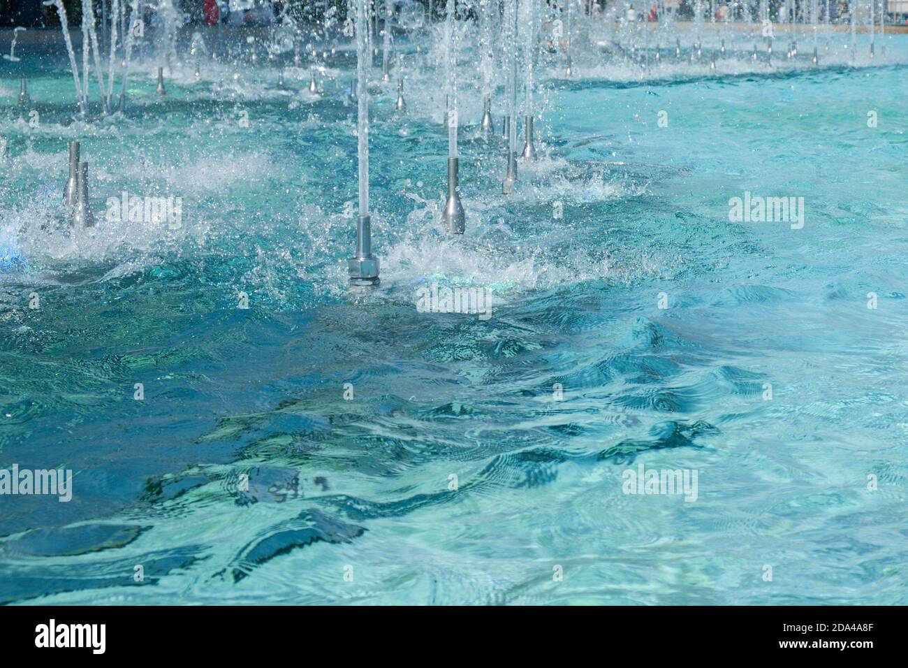 Smooth bore nozzles for foam jet water stream effect with splashes. Ripple and reflection on turquoise water surface of city fountain. Urban water fea Stock Photo