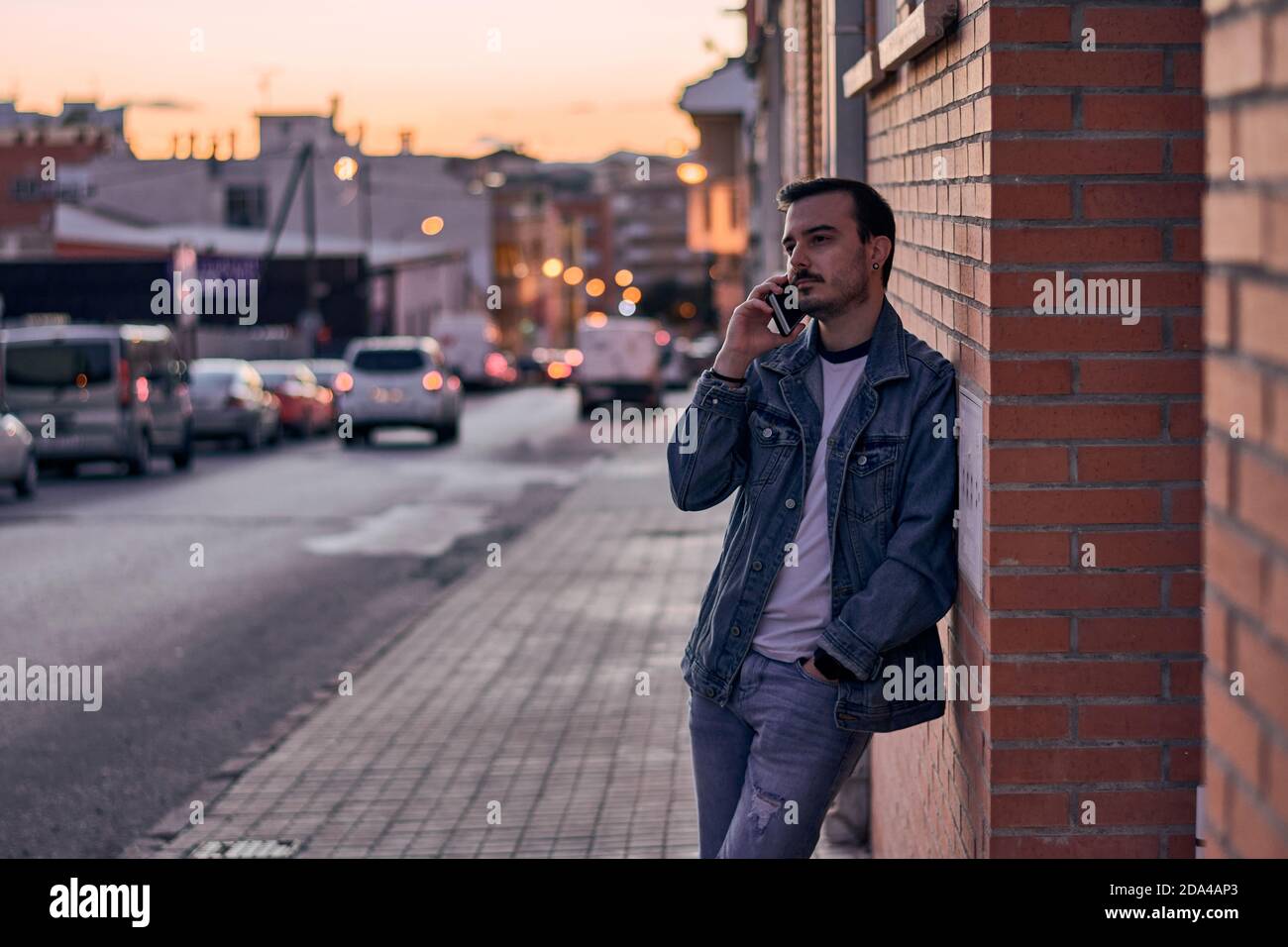 Young man talks on his phone leaning against a wall Stock Photo
