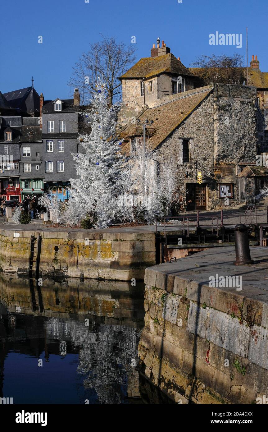 A white Christmas tree stands at the entrance to the Vieux Bassin, begun in the 1680s as a new harbour for the historic port of Honfleur in Calvados, Normandy, France.  Behind it is the Lieutenance, a group of buildings incorporating the former residence of the King’s Lieutenant and last vestiges of medieval ramparts built to defend Honfleur in the 13th and 14th centuries.  These include remnants of the Porte de Caen, one of the town’s two medieval gateways.  The other entrance, the Porte de Rouen, was demolished with the rest of the fortifications in the 17th century. Stock Photo