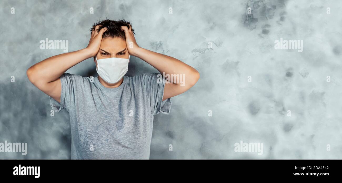 young girl holds her head in her hands. fatigue and anger from the coronavirus. white medical mask. Stock Photo