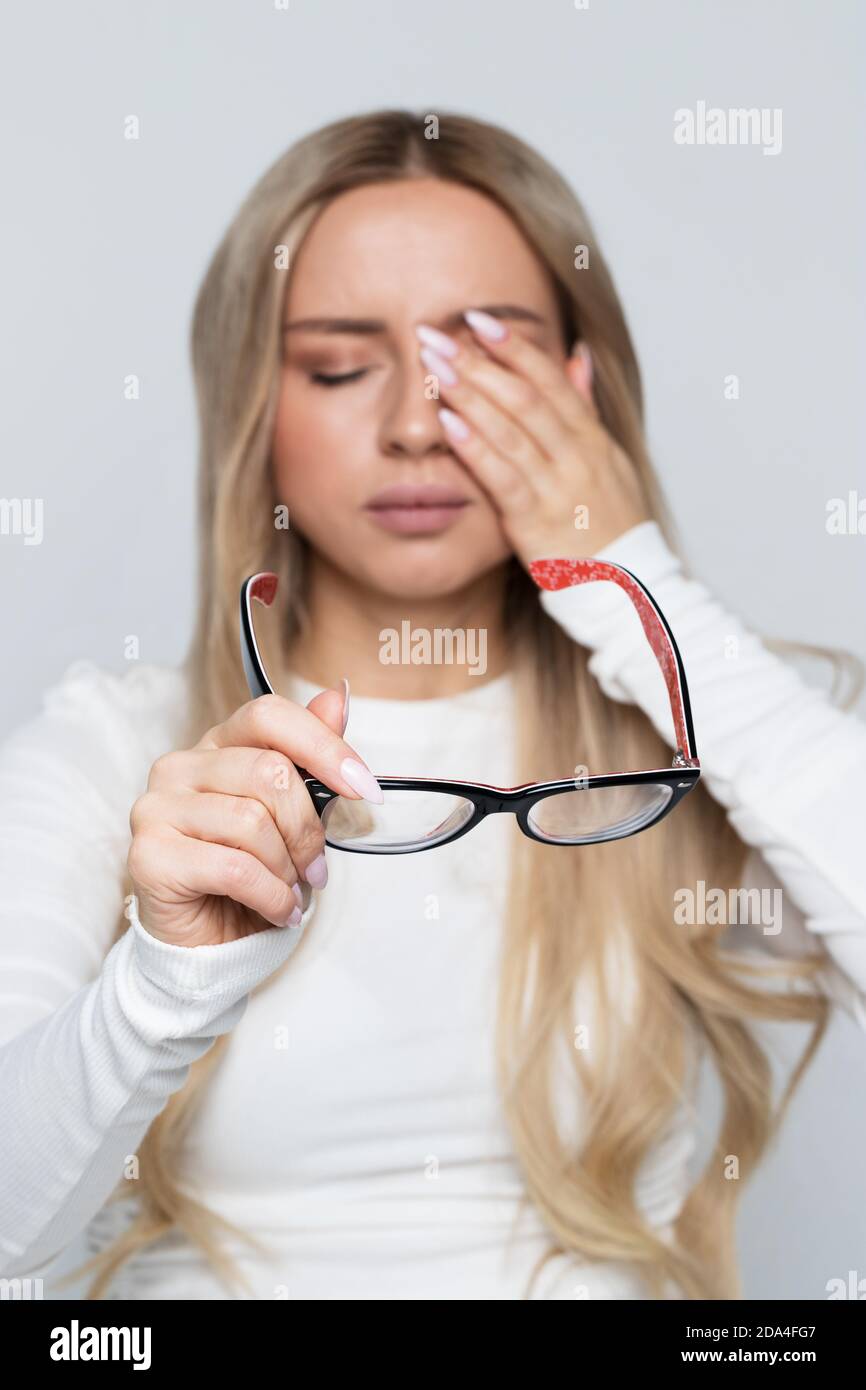 Woman with glasses holding in hand rubbing her eyes, feels tired after working on laptop, soft focus. Overwork concept. Exhausted and fatigue girl Stock Photo