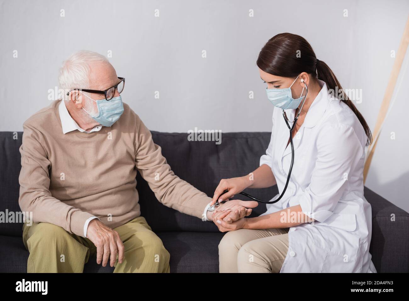 brunette nurse checking pressure of aged man with stethoscope Stock Photo