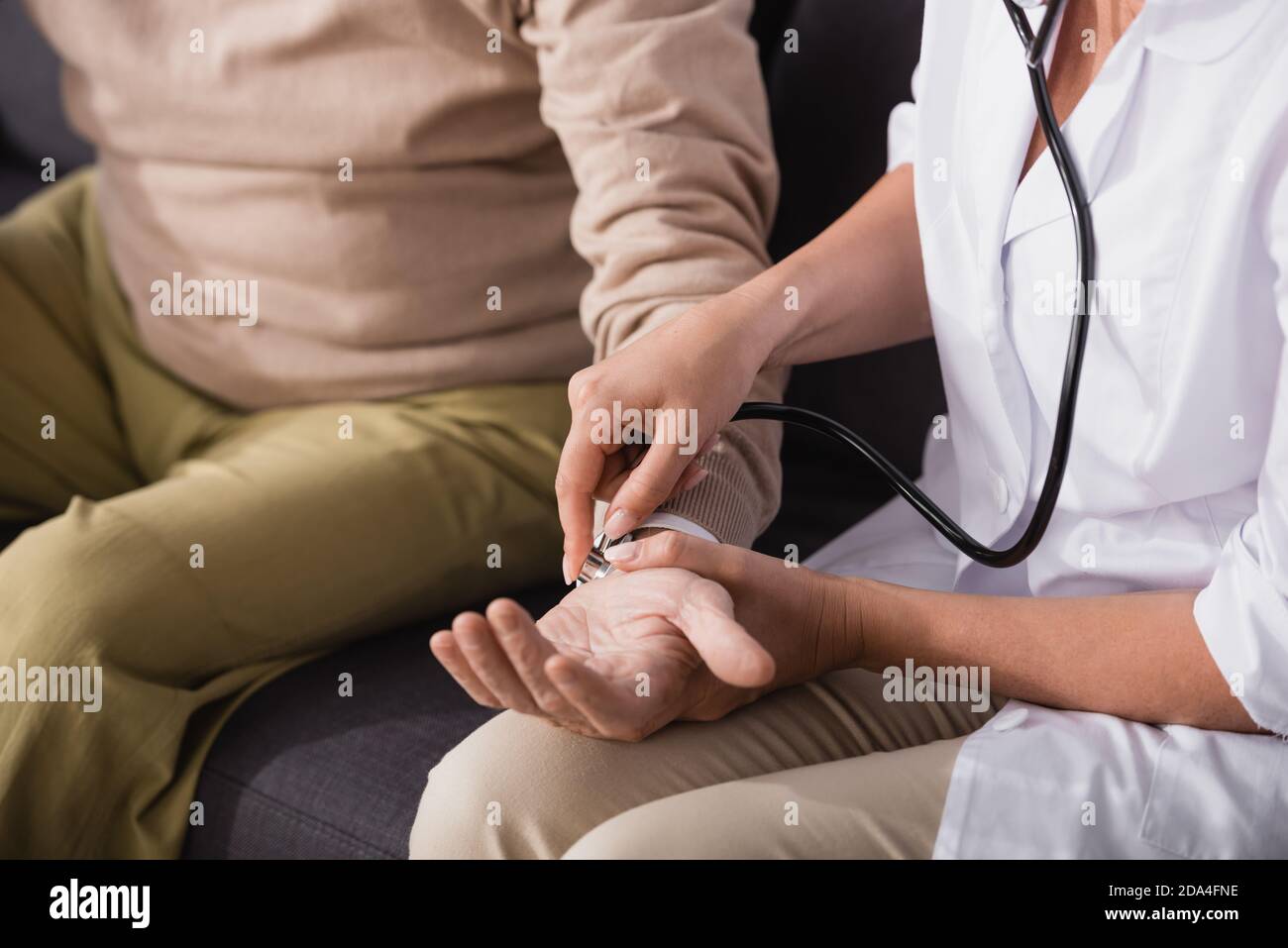 cropped view of social worker examining aged man with stethoscope on blurred background Stock Photo