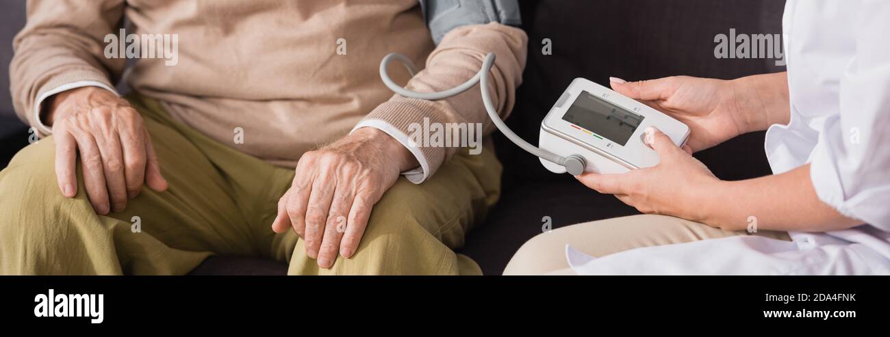 geriatric nurse examining aged man with tonometer at home, banner Stock Photo