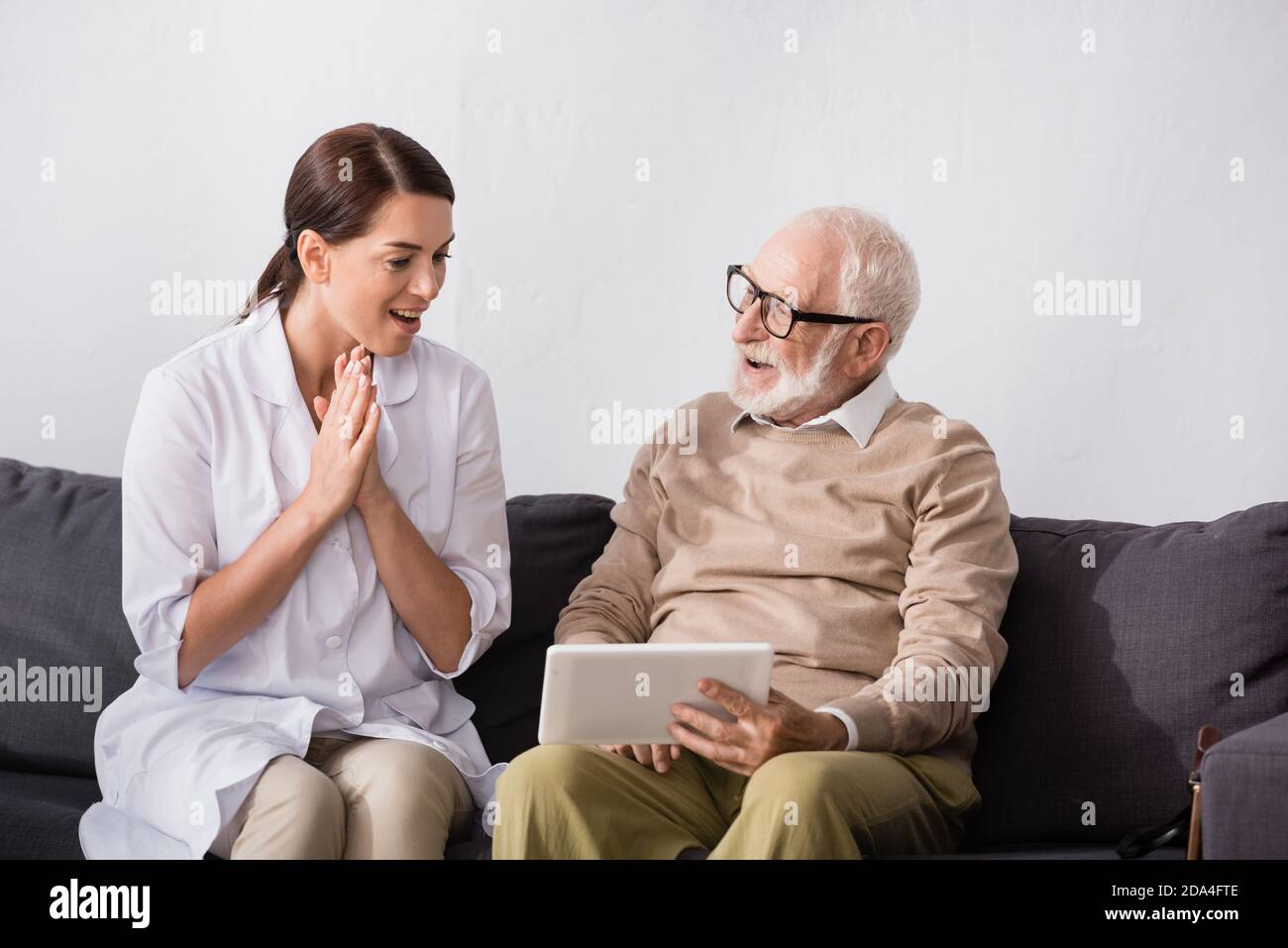brunette social worker showing wow gesture while looking at aged man holding digital tablet Stock Photo