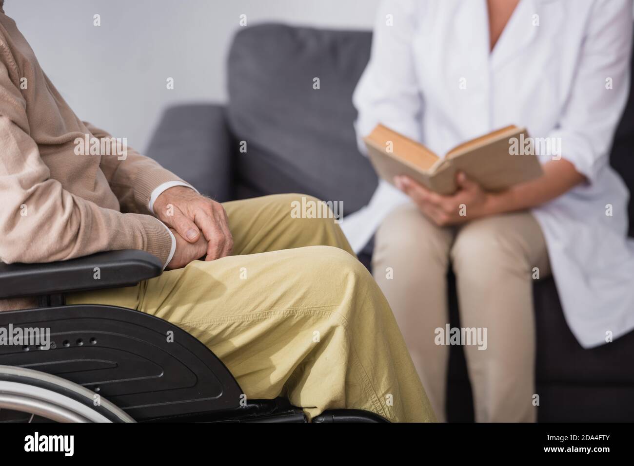 cropped view of geriatric nurse reading book to elderly man at home Stock Photo