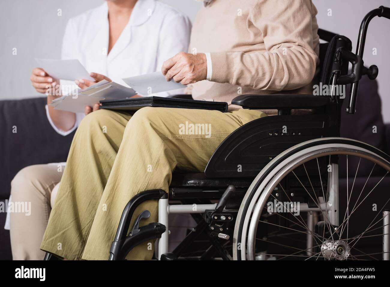 cropped view of social worker showing family photos to handicapped man on blurred background Stock Photo