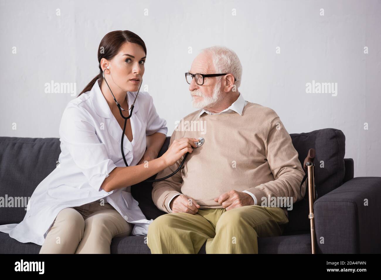 social worker checking health of aged patient with stethoscope Stock Photo