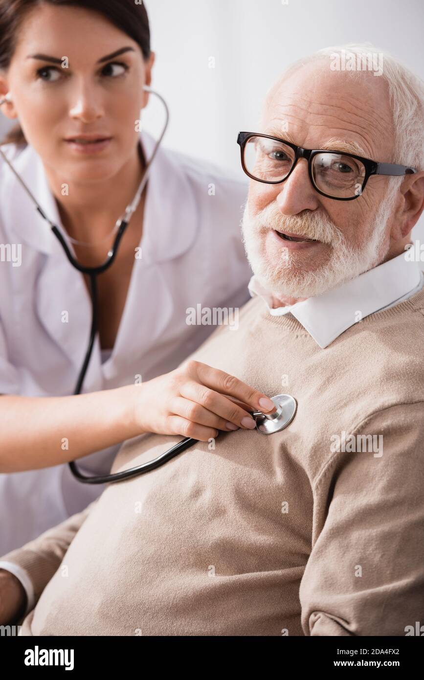 medical assistant examining aged man with stethoscope on blurred background Stock Photo