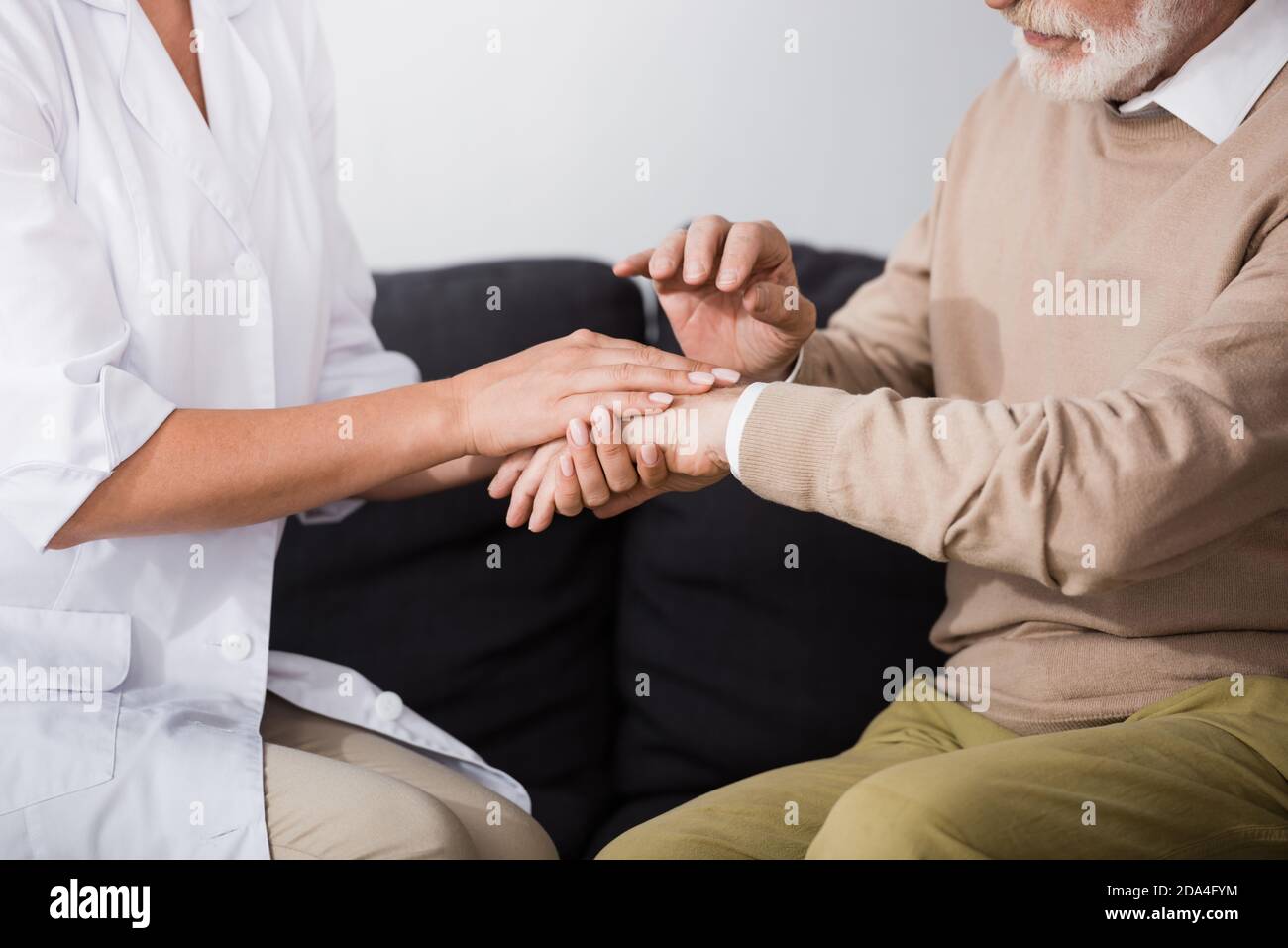cropped view of senior man and social worker holding hands while sitting on sofa at home Stock Photo