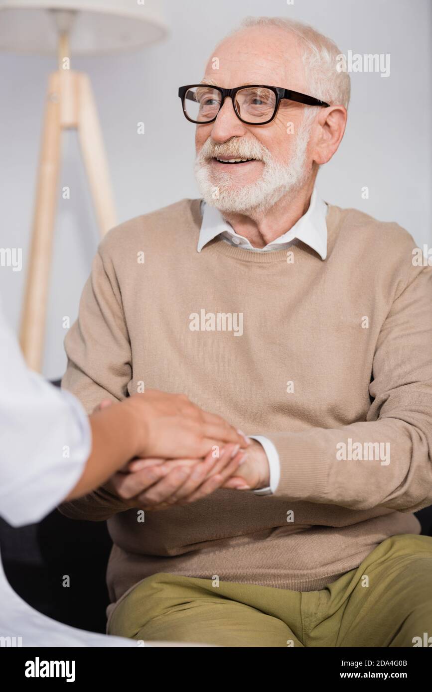 smiling senior man holding hands with social nurse at home on blurred foreground Stock Photo