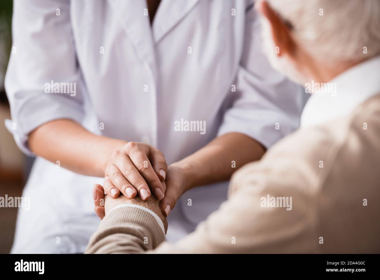 cropped view of social worker holding hands of aged man on blurred background Stock Photo