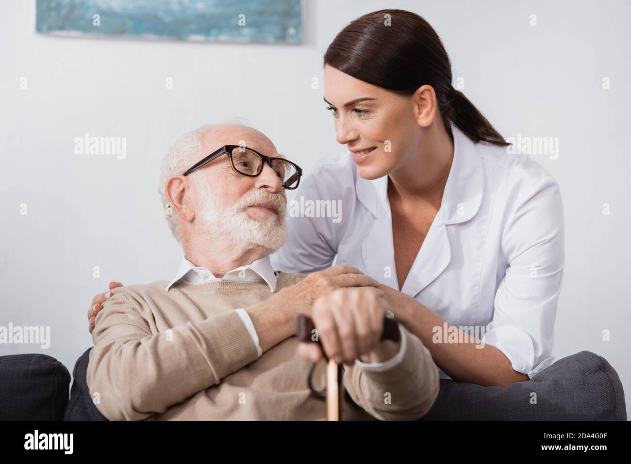 geriatric nurse and aged man looking at each other at home Stock Photo