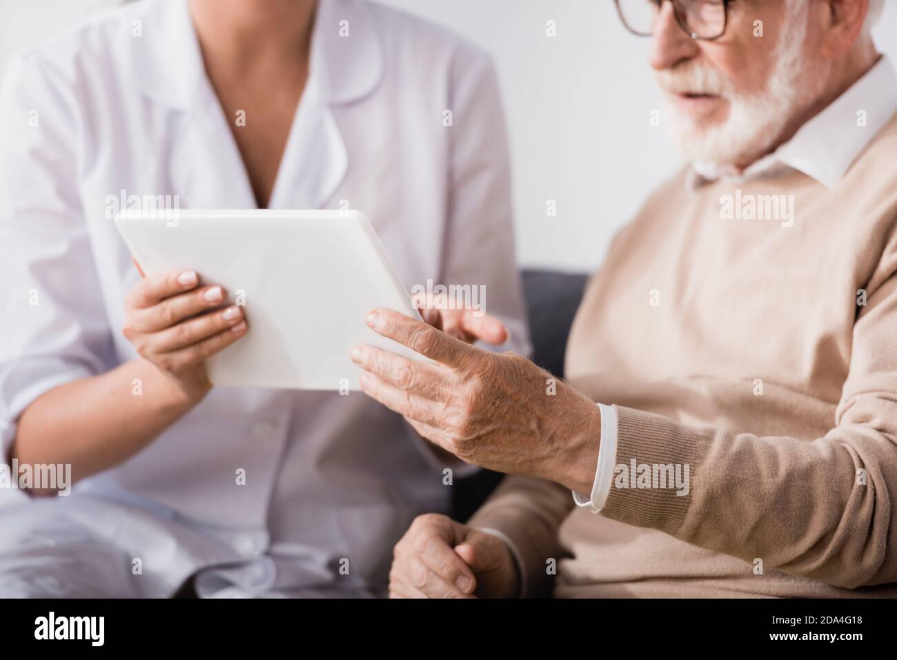 cropped of social worker showing digital tablet to aged man at home Stock Photo