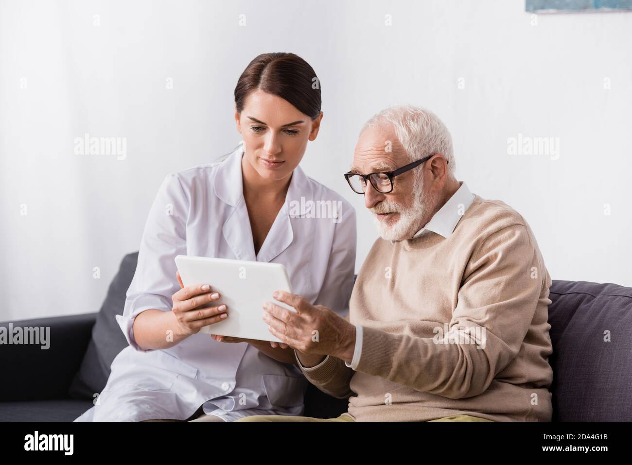brunette geriatric nurse and elderly man using digital tablet together Stock Photo