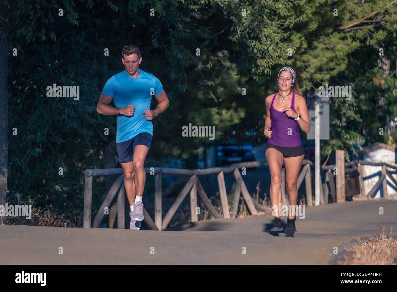 Young man in blue t-shirt and young woman in purple t-shirt jogging at park Stock Photo