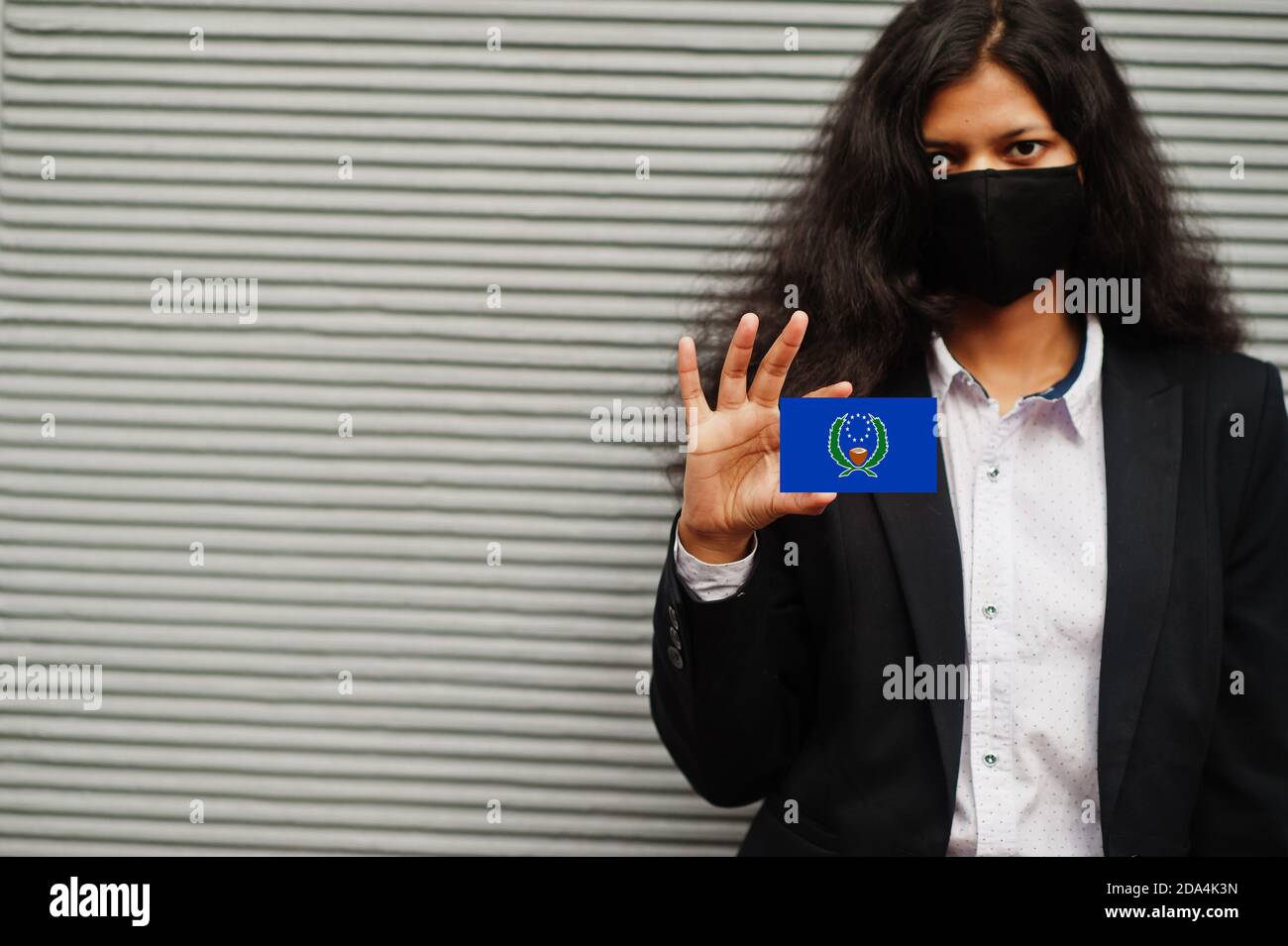 Asian woman at formal wear and black protect face mask hold Pohnpei flag at hand against gray background. Coronavirus at country concept. Stock Photo