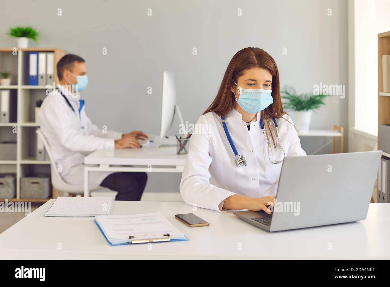 Doctors in medical face masks working on computers sitting at desks in the office Stock Photo