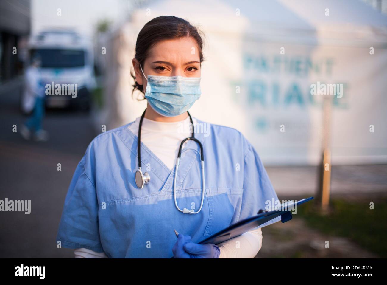 Portrait of very tired & exhausted UK NHS ICU doctor in front of hospital,emergency patient triage tent in background,Coronavirus COVID-19 pandemic Stock Photo