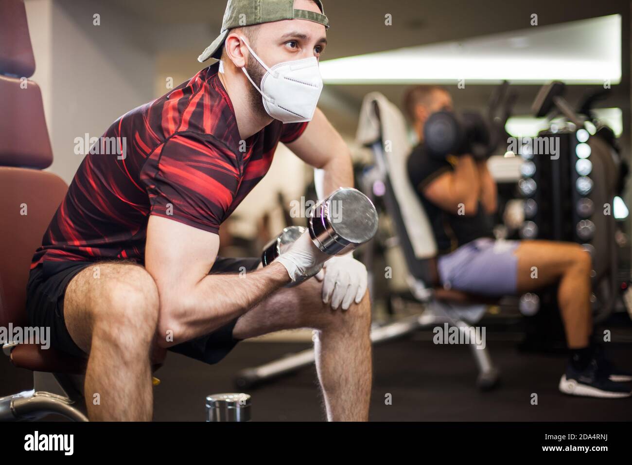 Young men working out wearing face mask & latex rubber gloves,performing bicep curl with dumbbells,COVID-19 pandemic social distancing rules Stock Photo