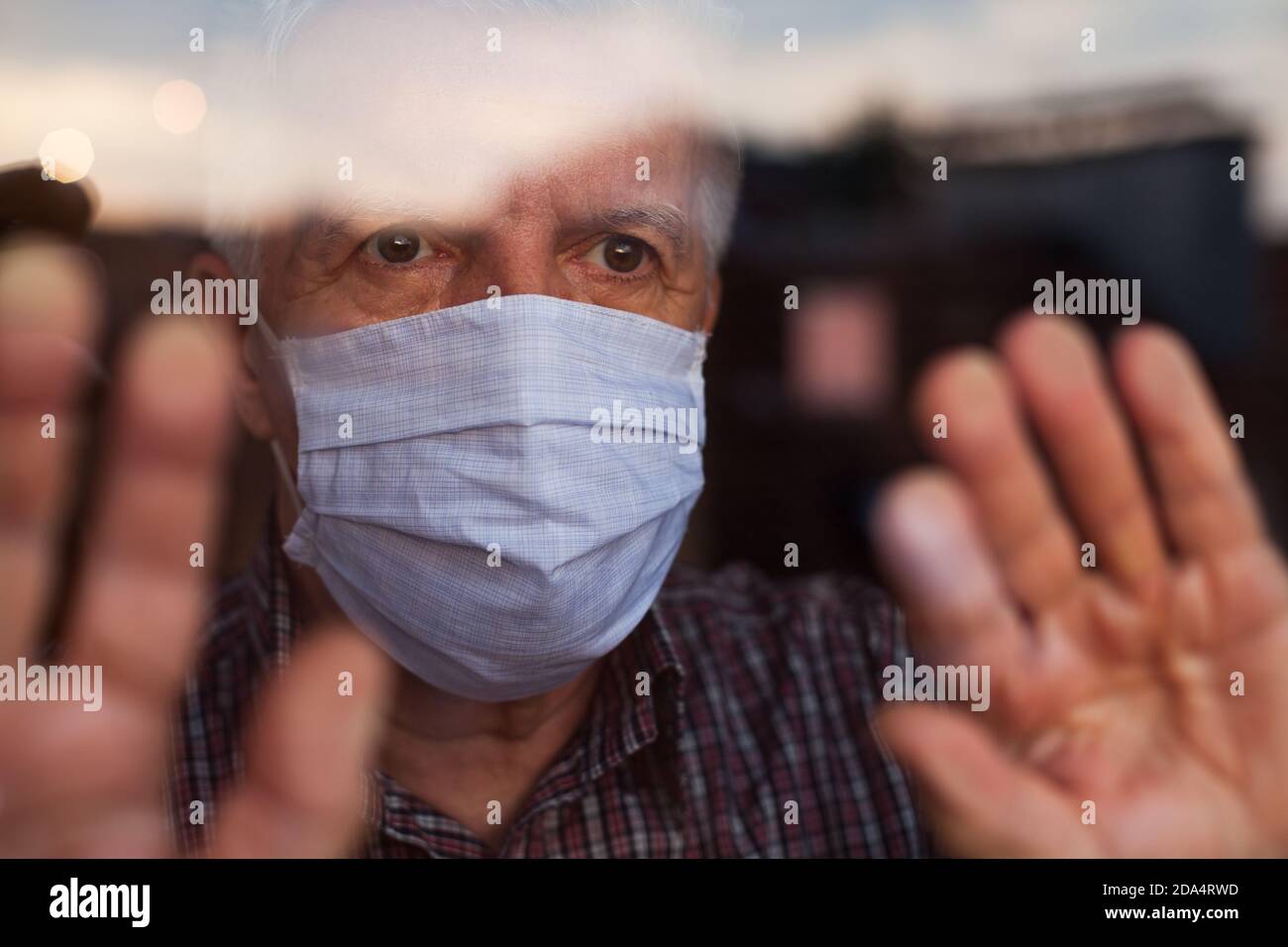 Elderly caucasian man wearing hand made protective face mask,in nursing care home,looking outside window, sadness,stress & hope in his eyes Stock Photo
