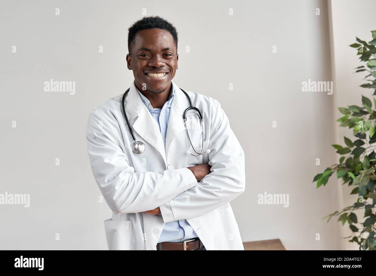 Happy african male doctor looking at camera standing at white wall. Stock Photo