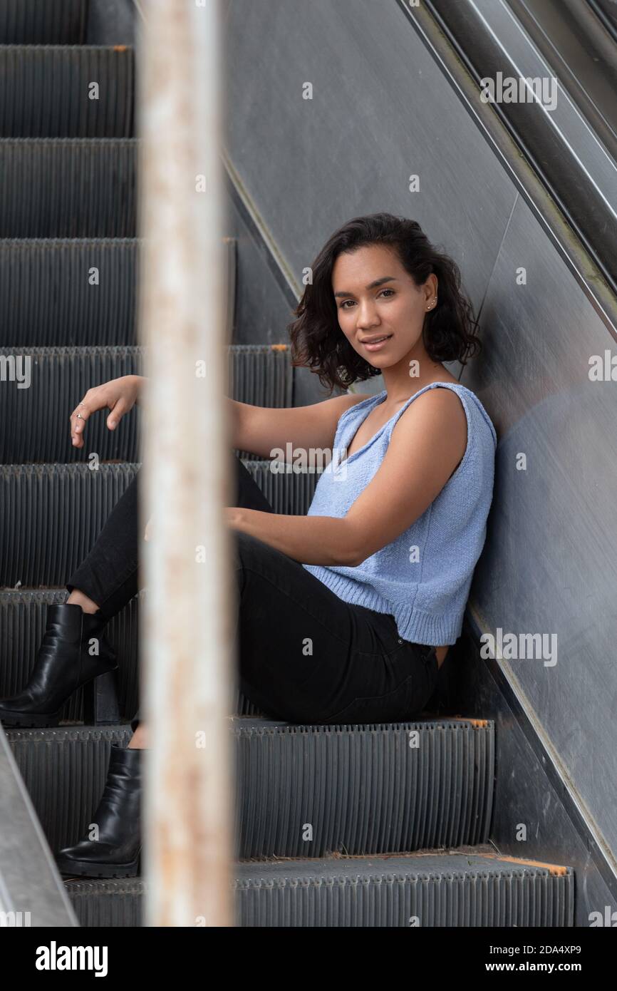 young brunette latina girl with short hair and curls, sitting on electric  stands, wearing blue blouse, black pants, casual style on the city Stock  Photo - Alamy