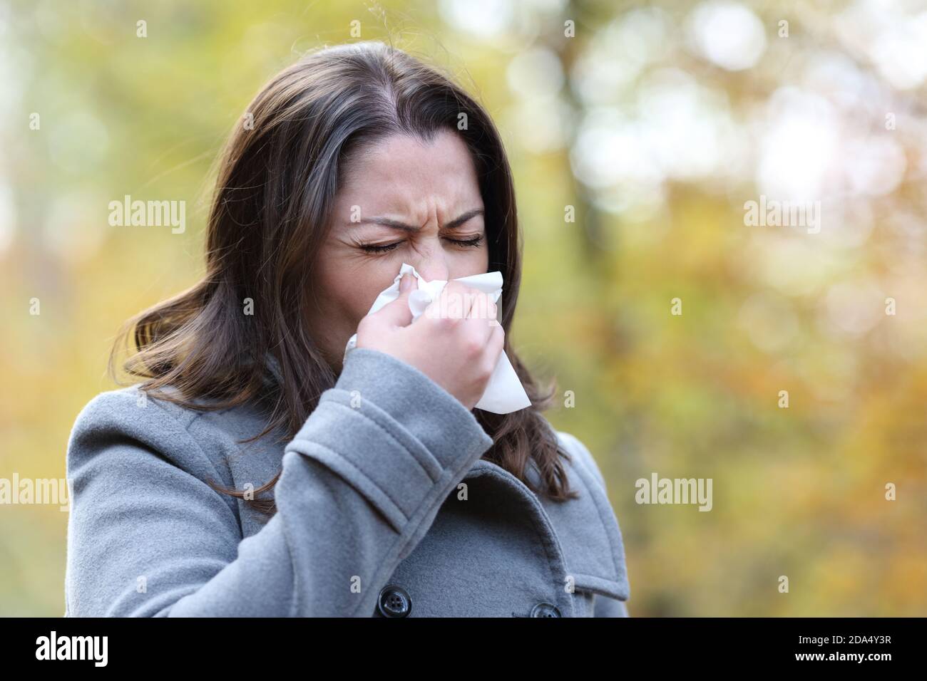 Ill woman with flu symptoms using tissue to blow walking in a park in winter Stock Photo