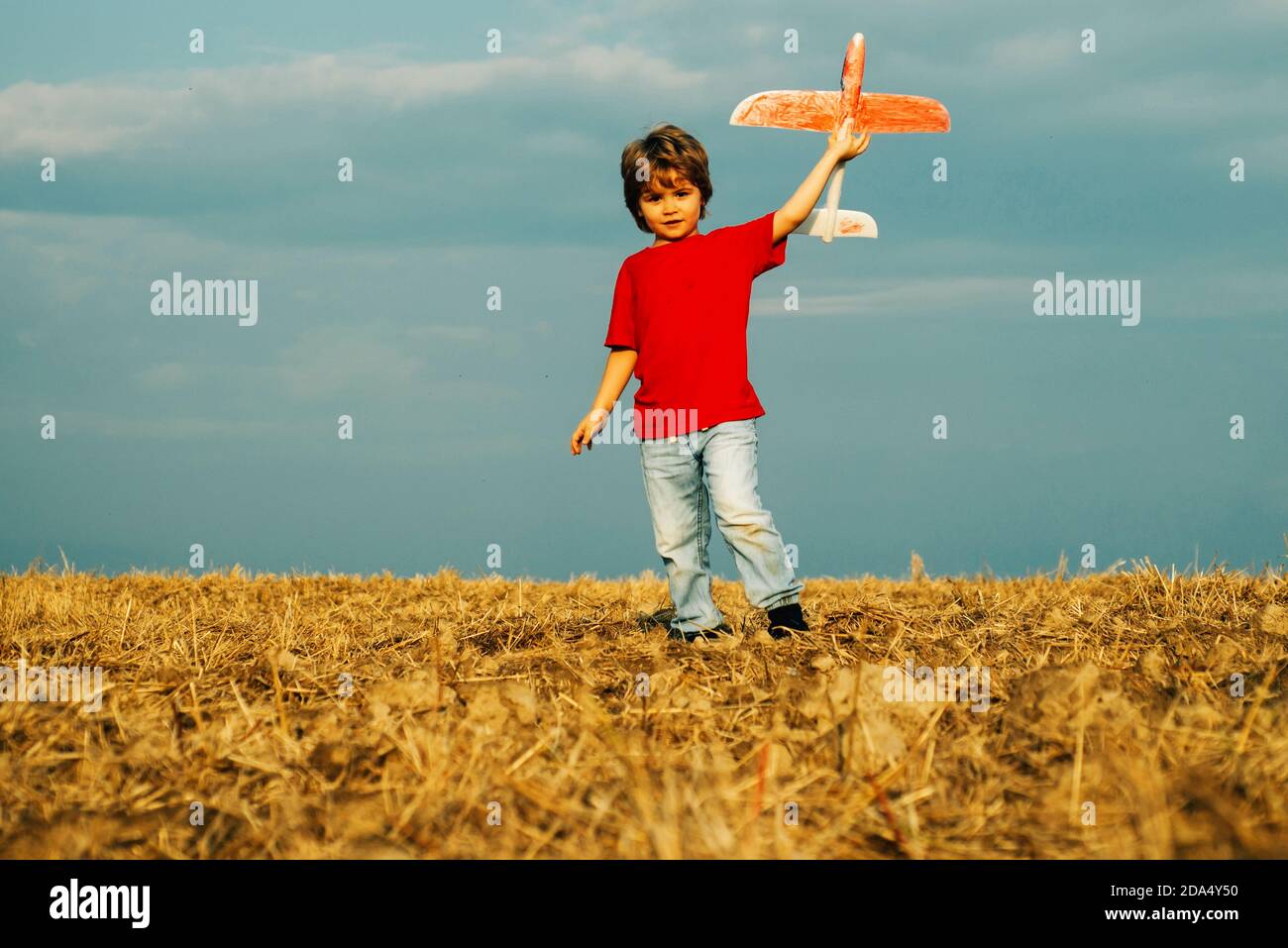 Little cute boy playing with a toy airplane. The concept of child kindness and childhood. Children run with plane on field. Child playing with model Stock Photo
