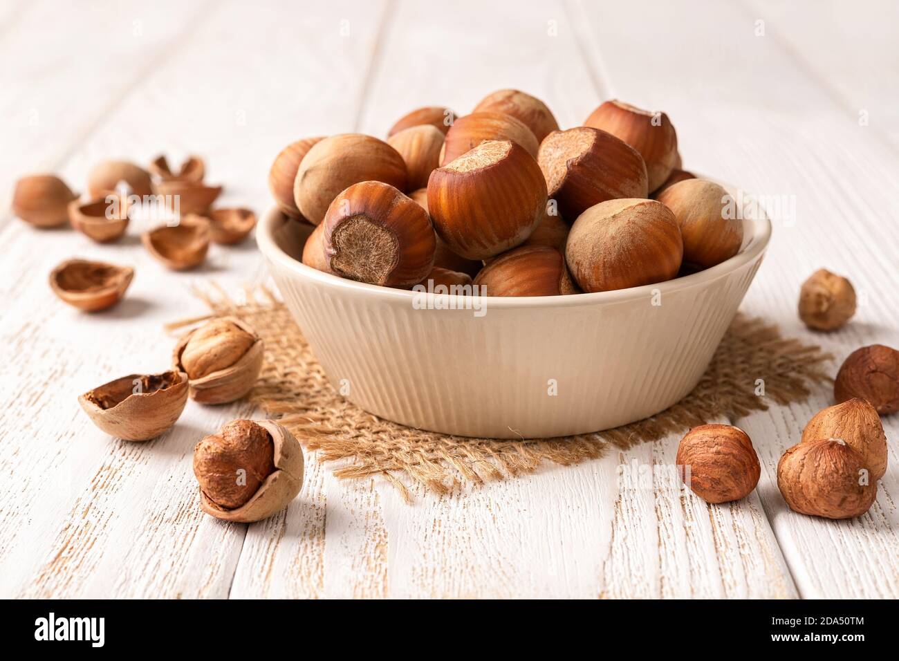 Hazelnuts in a beige ceramic bowl on a white wood table. Healthy vegetarian eating, antioxidant and protein source. Ketogenic and raw food diets. Stock Photo