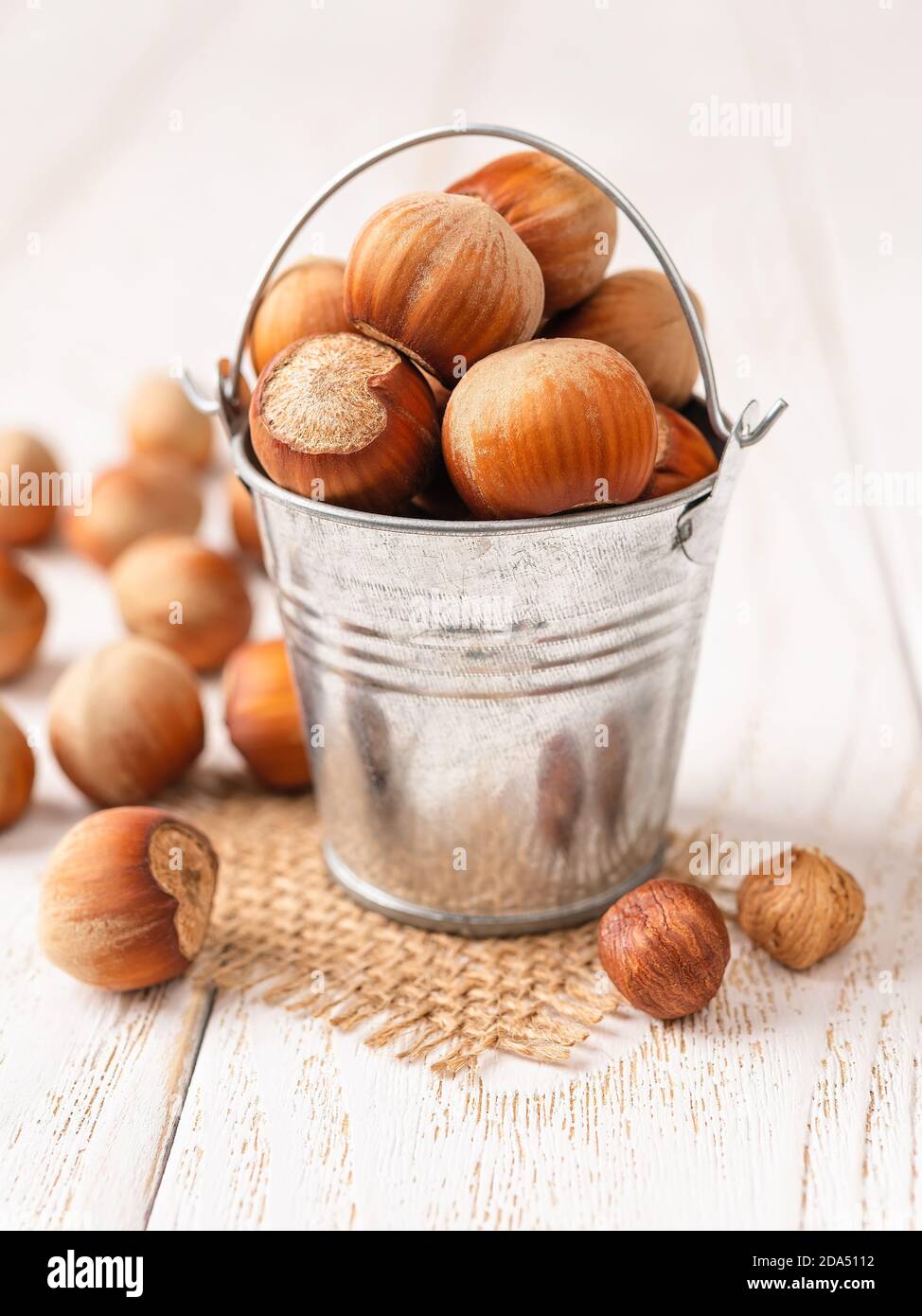 Hazelnuts in a small metal bucket over white wood table. Healthy vegetarian eating, antioxidant and protein source. Ketogenic and raw food diets. Crop Stock Photo