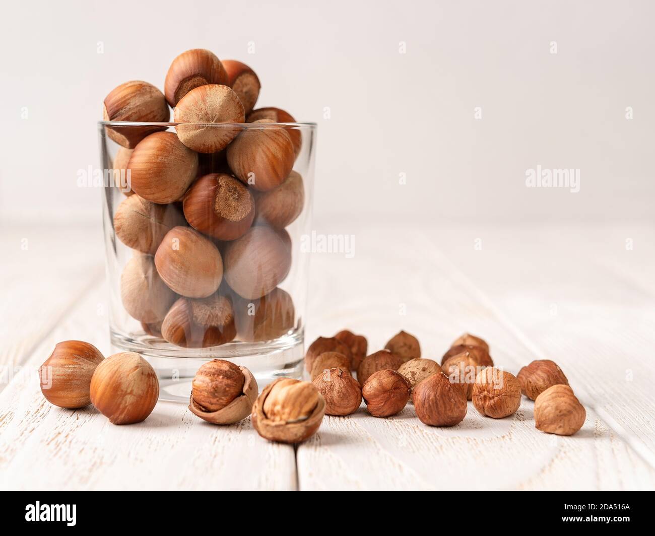 Whole hazelnuts in a glass over white wood table. Healthy vegetarian eating, antioxidant and protein source. Ketogenic and raw food diets ingredient. Stock Photo