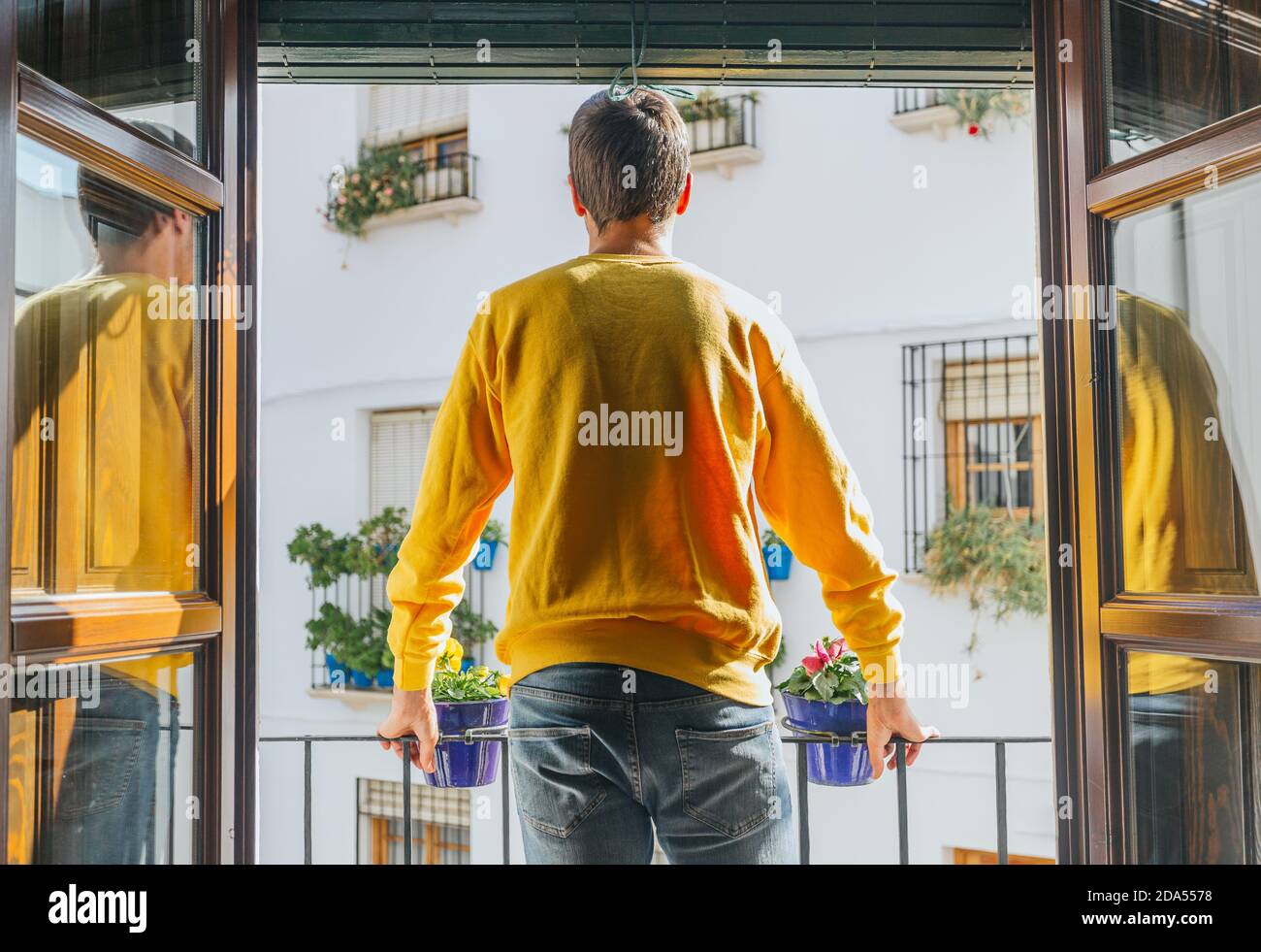 The boy standing on a balcony overlooking the street of potted windows with a yellow sweatshirt Stock Photo