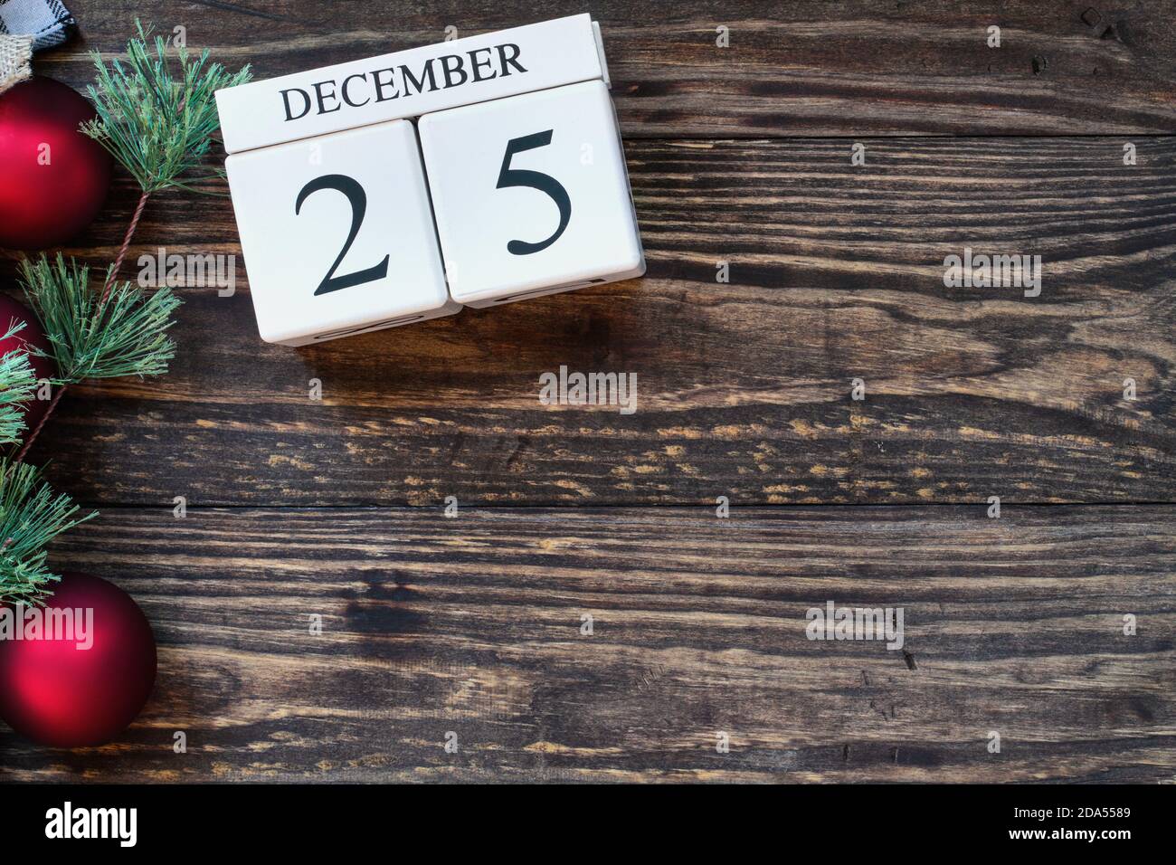 Wood calendar blocks with the date December 25th to mark Christmas Day with holiday trim of red ornaments and pine tree branch.. Top view with copy sp Stock Photo