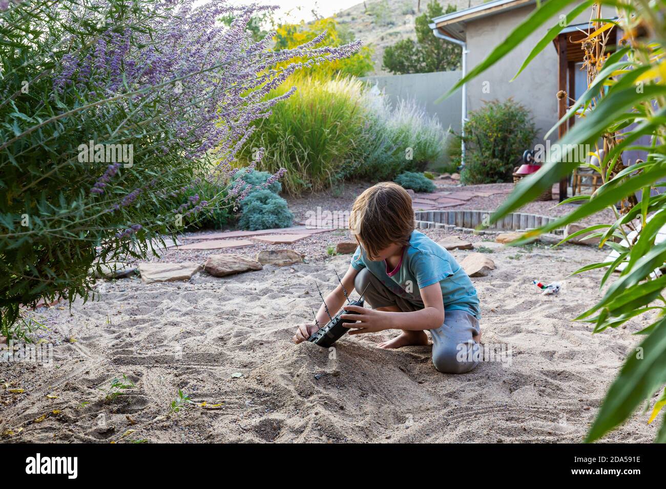 7 year old boy playing in sandy garden with his toy ship. Stock Photo